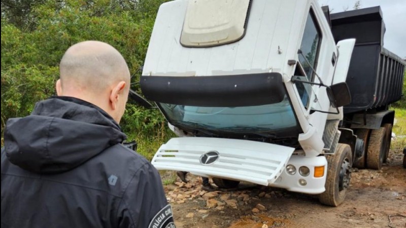 A imagem mostra um agente da Polícia Civil em frente a um caminhão caçamba apreendido