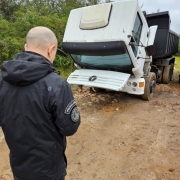 A imagem mostra um agente da Polícia Civil em frente a um caminhão caçamba apreendido