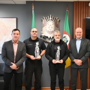 Comitiva retratada junto as representantes da SSP gaúcha em frente ao brasão e à bandeira do Estado do Rio Grande do Sul