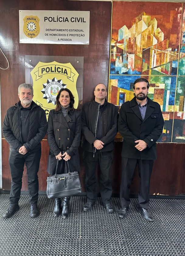 Quatro pessoas fotografadas em frente ao brasão da Polícia Civil no Departamento Estadual de Homicídios e Proteção à Pessoa (DHPP/PC)