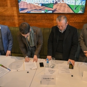 A imagem mostra o governador Eduardo Leite assinando o termo de cooperação. À esquerda está o prefeito de Passo Fundo, Pedro Almeida. À direita, estão o secretário adjunto Mário Ikeda e o chefe de Polícia Heraldo Guerrero