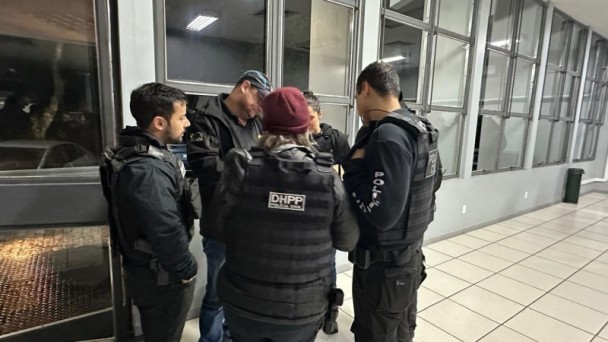 Cinco agentes da Polícia Civil se reúnem, duas mulheres e três homens. Uma delas veste um gorro na cor bordô.