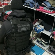 Agente fardado com identificação do DEIC vasculha prateleiras de roupas e calçados