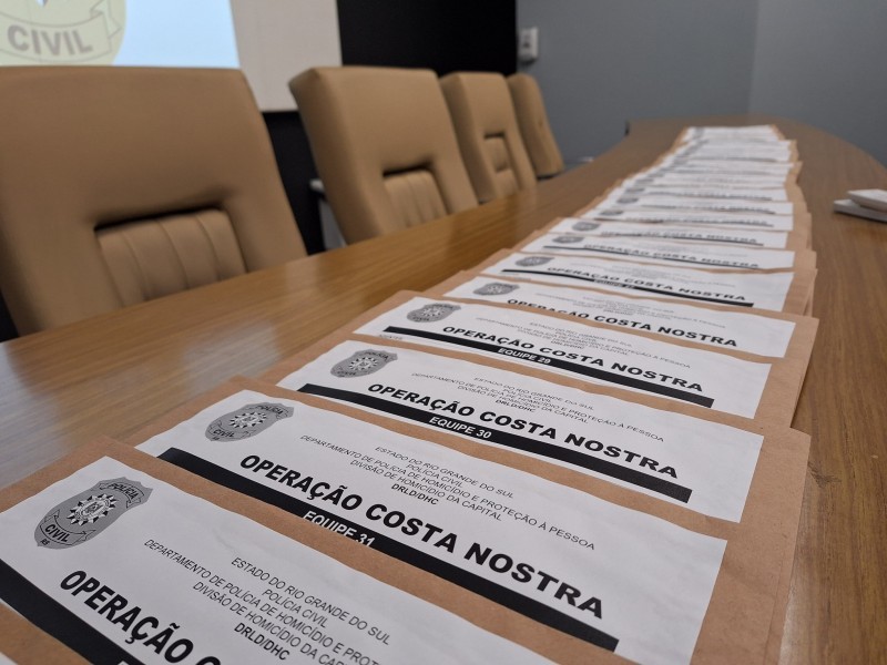 A imagem mostra envelopes com ordens judiciais referentes à Operação Costa Nostra. Os envelopes estão dispostos sobre uma ampla mesa