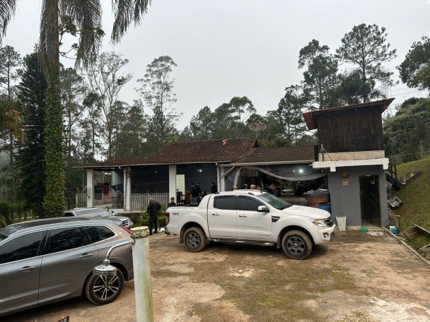 Camionete e carros estacionados em frente a uma casa da zona rural.