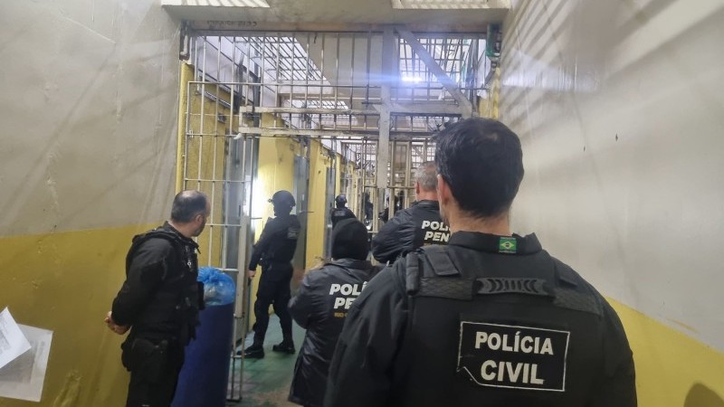Na imagem seis policiais aparecem de costas entrando em uma unidade prisional