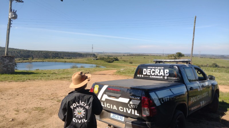 Policial parado e camionete da Decrab estacionada em frente a um a&ccedil;ude.