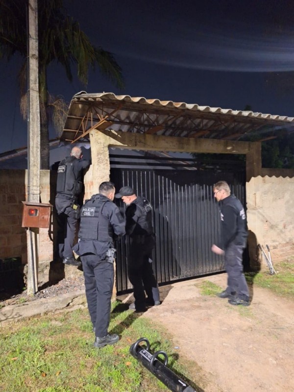 Quatro agentes da Polícia Civil em frente a um portão de uma casa