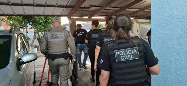 Um grupo de policiais da “POLÍCIA CIVIL” e da “BRIGADA MILITAR” entra em uma área residencial. Eles usam equipamentos táticos e estão acompanhados por um cão policial. O cenário mostra uma garagem coberta com um carro estacionado, árvores e uma casa com roupas estendidas no varal. A cena transmite uma ação coordenada de segurança ou investigação