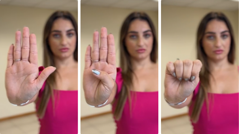 Mulher vestida de pink e cabelos longos faz sequ&ecirc;ncia de gestos para pedir socorro: - no primeiro quadro, a m&atilde;o est&aacute; aberta, com a palma voltada para frente. Os dedos est&atilde;o estendidos e juntos, enquanto o polegar aparece levemente dobrado para dentro. &Eacute; um gesto claro de abertura e exposi&ccedil;&atilde;o da palma; - no segundo quadro, o polegar &eacute; dobrado para dentro da palma, enquanto os outros quatro dedos permanecem estendidos e juntos. Esse movimento marca o in&iacute;cio de um fechamento da m&atilde;o; no terceiro quadro, todos os dedos se fecham sobre o polegar, formando um punho. A m&atilde;o est&aacute; completamente fechada, com o polegar preso dentro.