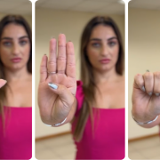 Mulher vestida de pink e cabelos longos faz sequ&ecirc;ncia de gestos para pedir socorro: - no primeiro quadro, a m&atilde;o est&aacute; aberta, com a palma voltada para frente. Os dedos est&atilde;o estendidos e juntos, enquanto o polegar aparece levemente dobrado para dentro. &Eacute; um gesto claro de abertura e exposi&ccedil;&atilde;o da palma; - no segundo quadro, o polegar &eacute; dobrado para dentro da palma, enquanto os outros quatro dedos permanecem estendidos e juntos. Esse movimento marca o in&iacute;cio de um fechamento da m&atilde;o; no terceiro quadro, todos os dedos se fecham sobre o polegar, formando um punho. A m&atilde;o est&aacute; completamente fechada, com o polegar preso dentro.
