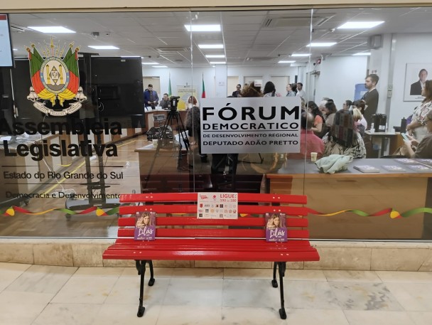 Na imagem o banco vermelho, símbolo de combate à violência contra as mulheres, em frente ao local da Audiência