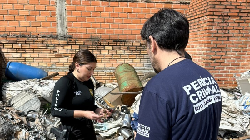 A imagem mostra dois servidores das for&ccedil;as de seguran&ccedil;a do Estado, uma mulher e um homem, analisando um material apreendido durante a opera&ccedil;&atilde;o 